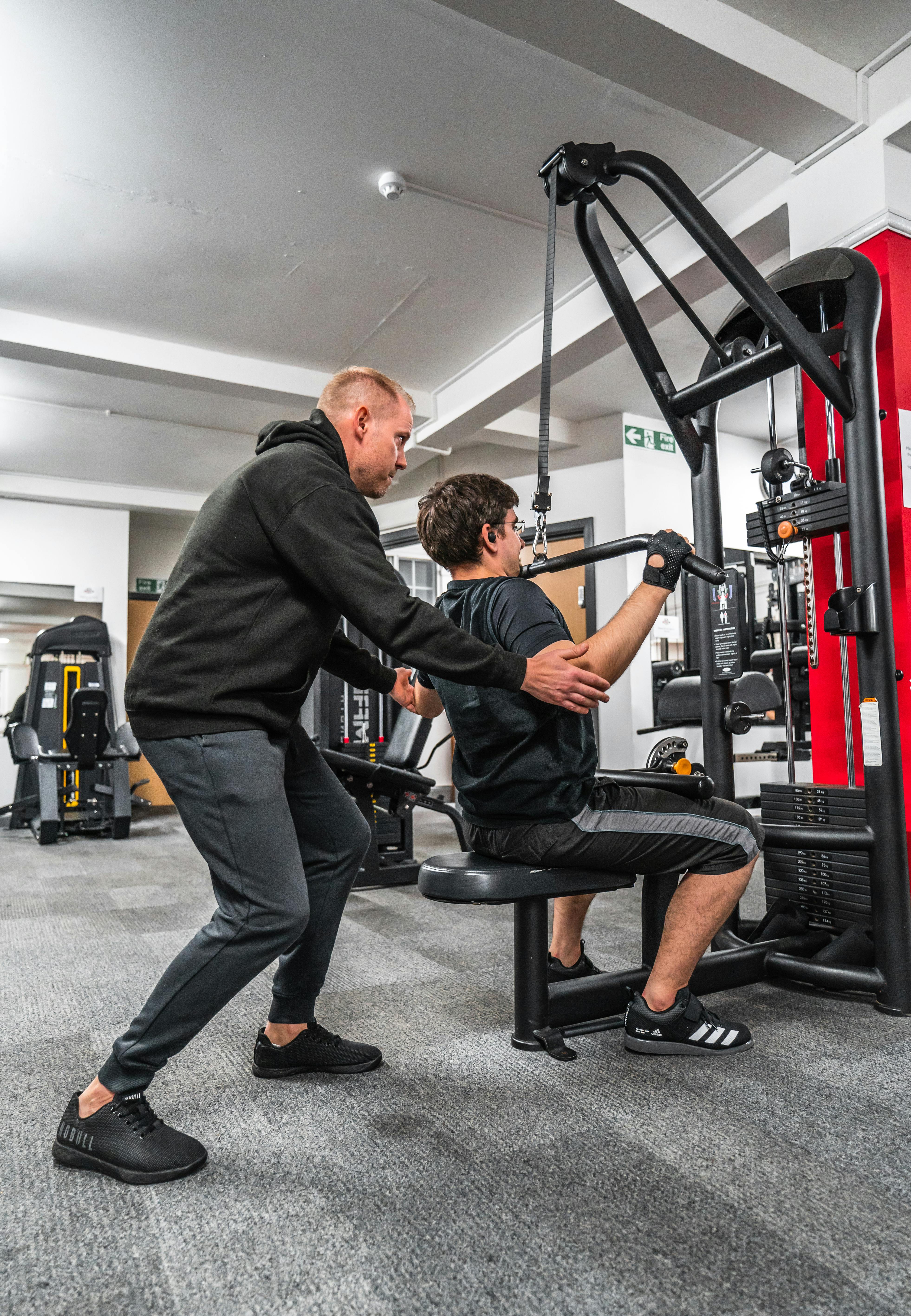 Personal trainer guiding a client through a machine-based strength exercise.