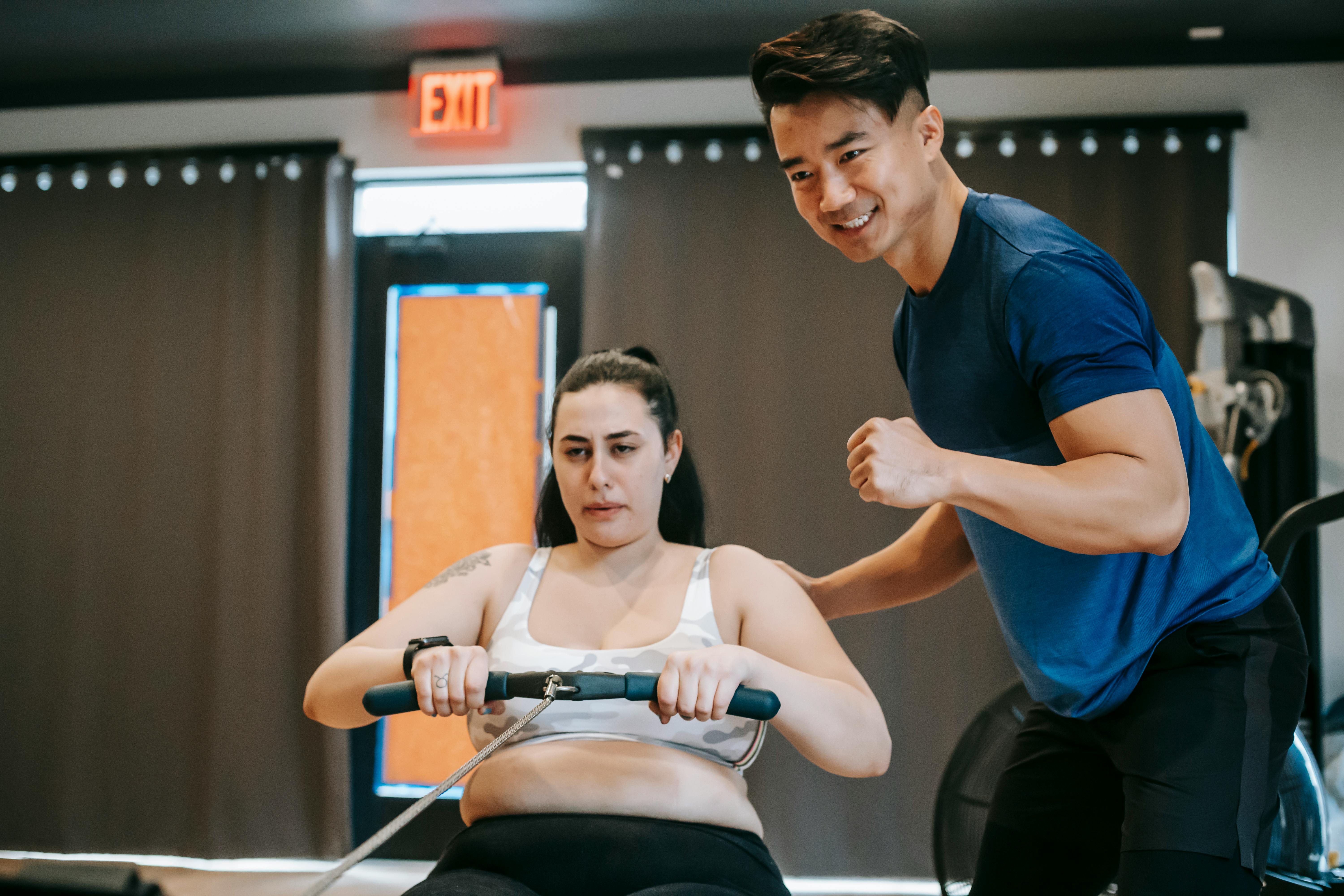Trainer supporting a client during a rowing-machine conditioning session.